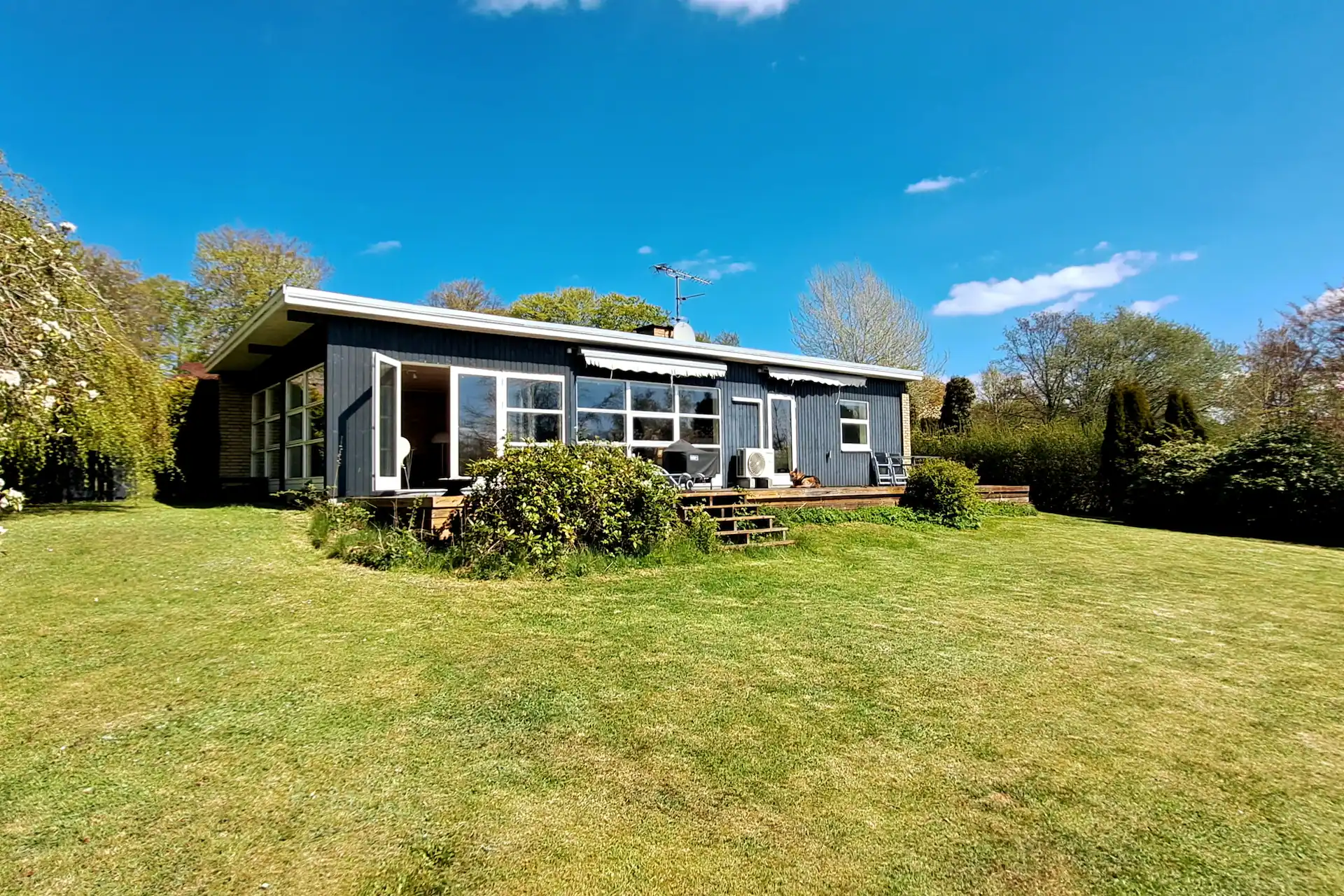 Sommerhusets træterrasse med åbne døre og havemøbler